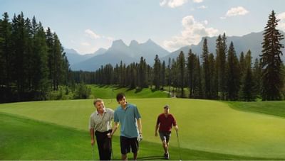 Three men walking across Silvertip Golf Course, surrounded by trees and majestic mountain near Clique Hotels & Resorts