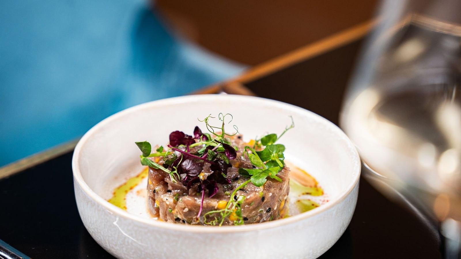 Beef tartare with microgreens in a white bowl by a wine glass in Seminars & Banquets at Warwick Paris Champs Elysées