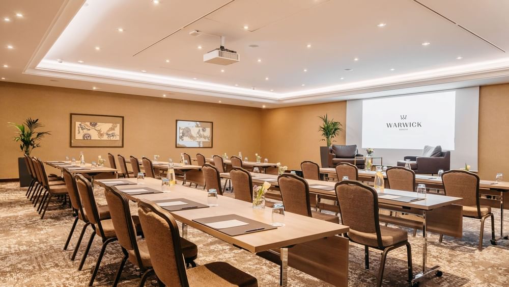 Long wooden desks by rows of chairs under a ceiling projector in Mont-Blanc + Jura at Warwick Geneva