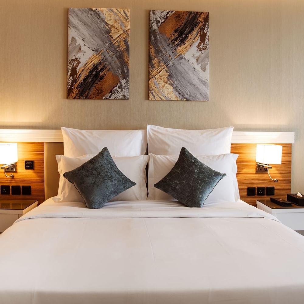 Plush bed with grey cushions by wooden nightstands in Superior King / Queen Room at Cantonal Hotel by Warwick Riyadh
