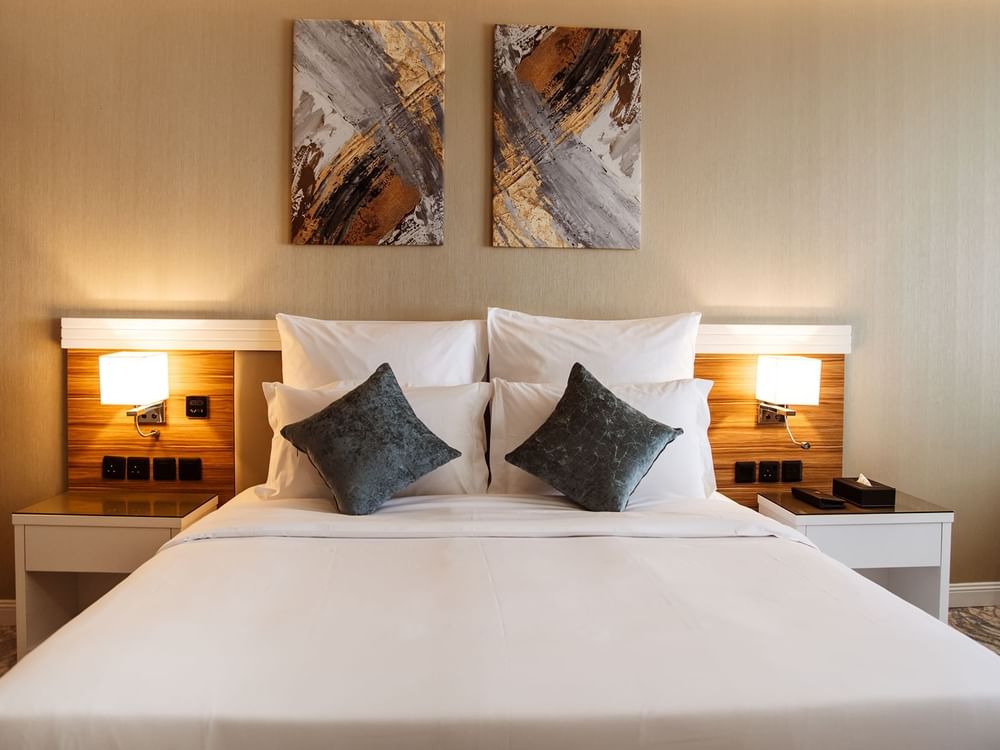 Double bed with white linens by wooden headboards in Standard King Room at Cantonal Hotel by Warwick Riyadh