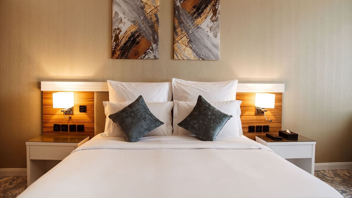 Plush bed with grey cushions by wooden nightstands in Superior King / Queen Room at Cantonal Hotel by Warwick Riyadh