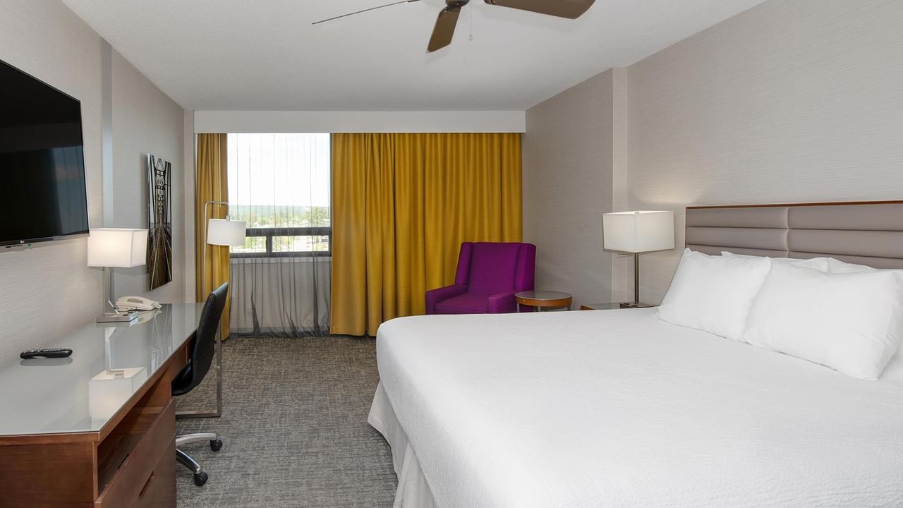 Coast King room with king bed, purple accent chair, work desk, and yellow curtains at Coast Prince George Hotel.