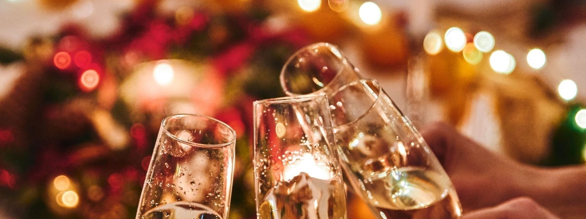 Three champagne flutes toasting over a festive Christmas Day Lunch table with warm lights and holiday decorations.