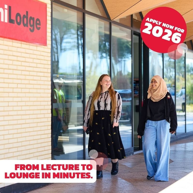 Two women walk past a UniLodge sign with an ad for 2026 applications.