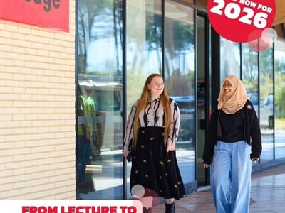 Two women walk past a UniLodge sign with an ad for 2026 applications.