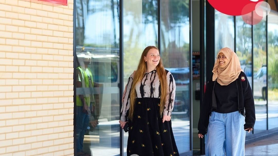 Two women walk past a UniLodge sign with an ad for 2026 applications.