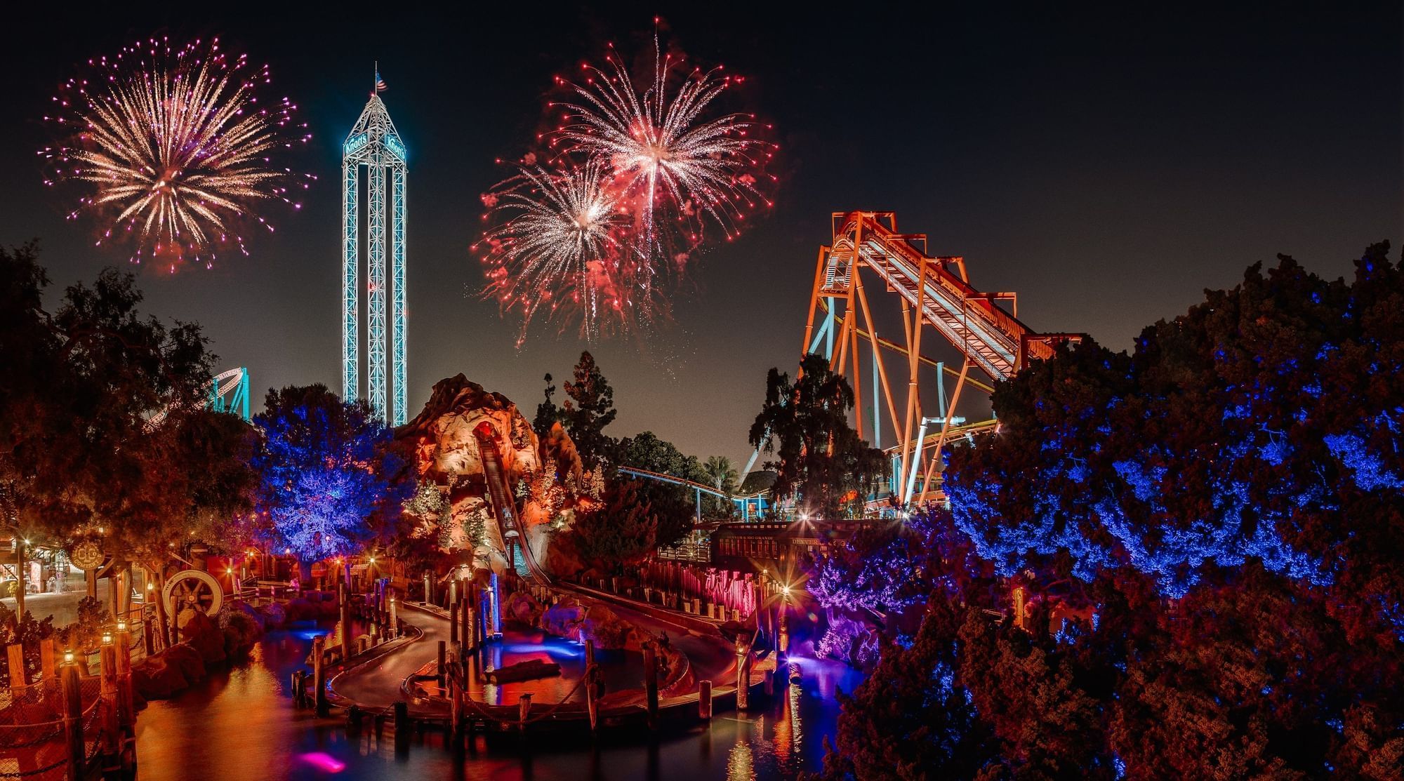 A nighttime view of a theme park with fireworks exploding in the sky.