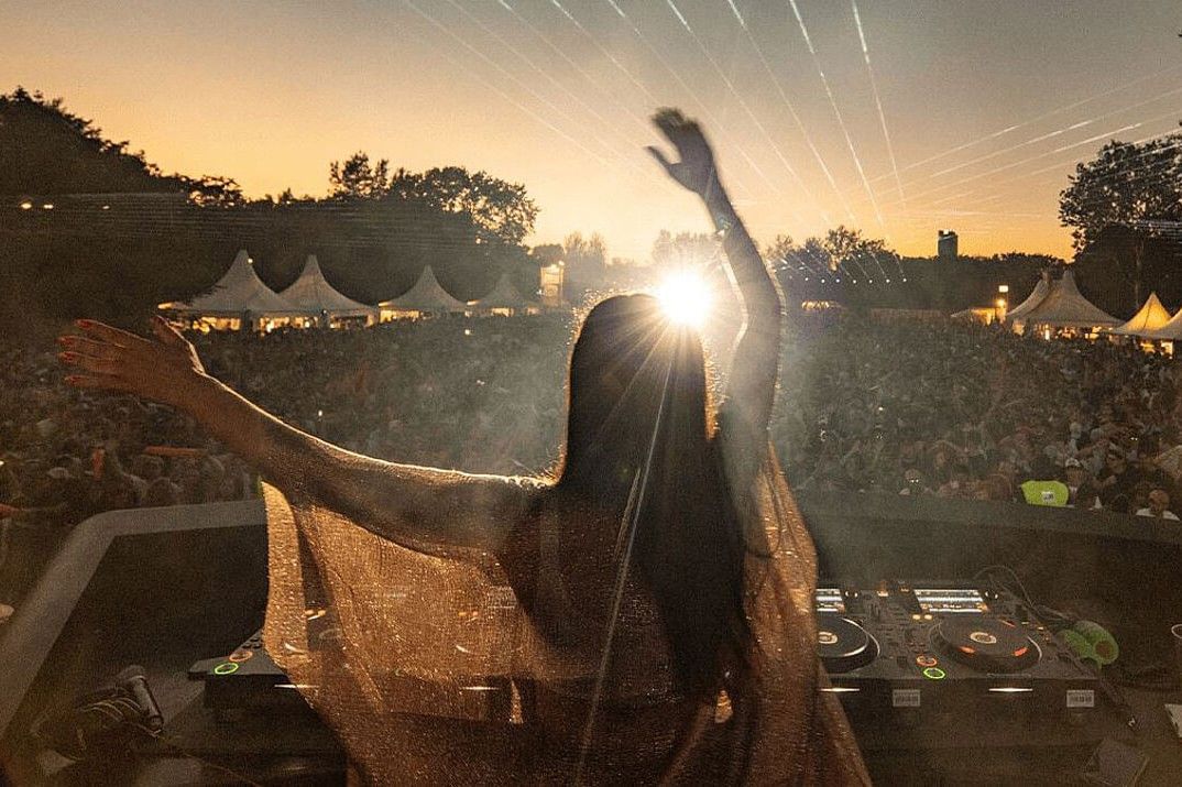 DJ begeistert die Menge beim Donauinselfest in Wien mit energiegeladener Musik und sommerlicher Festivalstimmung bei Sonnenuntergang.