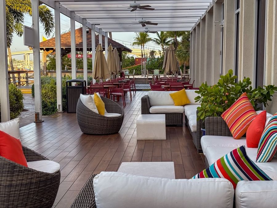 Wicker chairs by white sofas under a pergola surrounding colorful pillows in Verandah at Warwick Paradise Island Bahamas