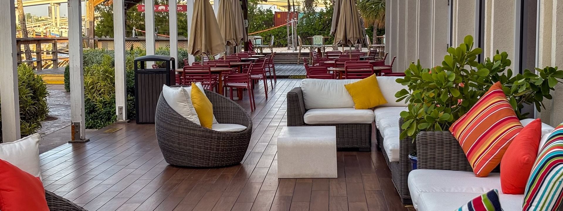 Wicker chairs by white sofas under a pergola surrounding colorful pillows in Verandah at Warwick Paradise Island Bahamas