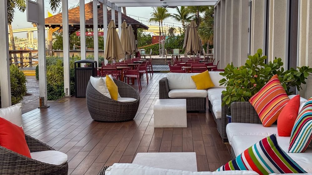 Wicker chairs by white sofas under a pergola surrounding colorful pillows in Verandah at Warwick Paradise Island Bahamas