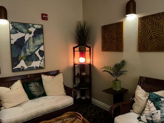 Two wicker chairs, one with pillows, a side table with a plant, and wall art in a cozy room.