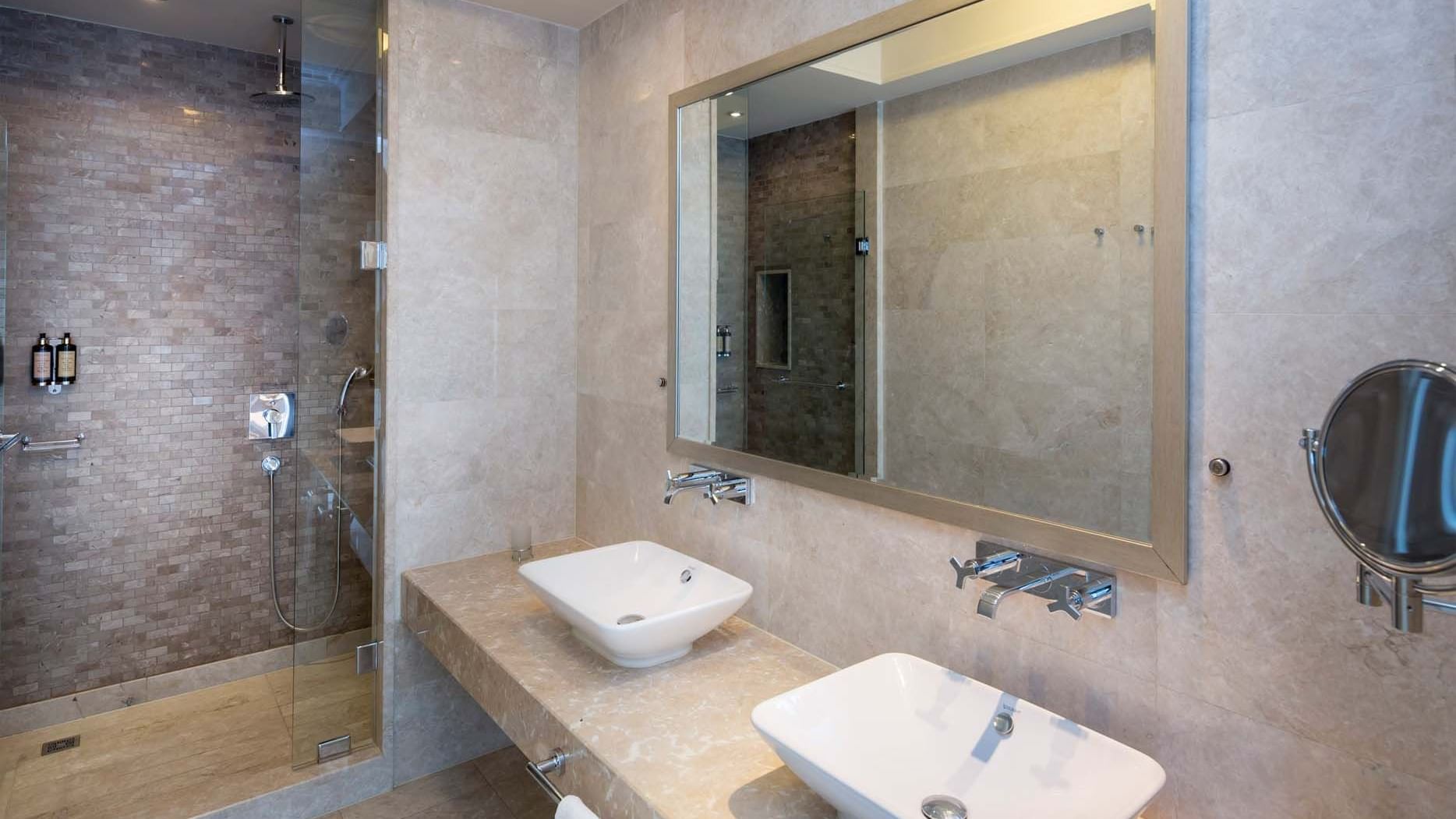 Titanic Business Kartal'ın Premier Suite'inde, iki seramik lavaboya sahip şık bir banyo tezgahı ve modern bir duş alanı ile konforlu bir banyo deneyimi sunuluyor.