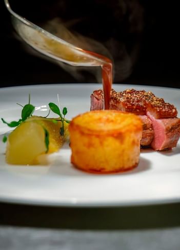Close-up of pink beef, golden soufflé, and sauce poured over the meat at The Saujana Hotel Kuala Lumpur