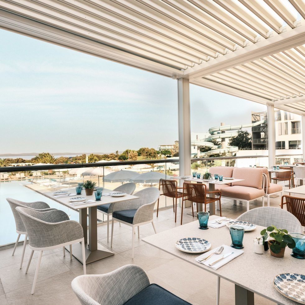 Terrassenrestaurant mit modernen Möbeln, Glaswänden und Blick auf Pool und Rutsche.