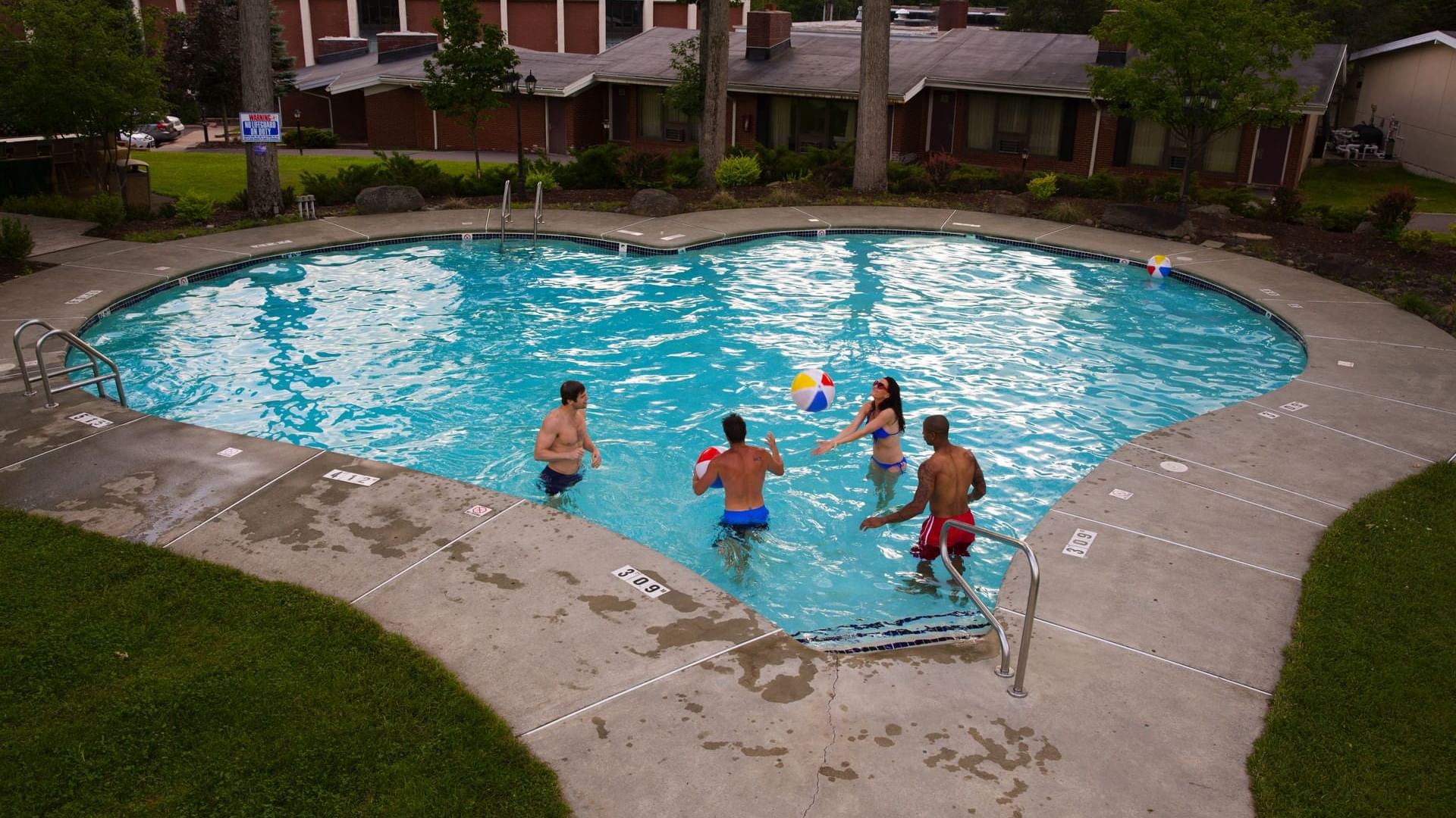 Group of friends playing in the heart shaped outdoor pool with a beach ball at Cove Pocono Resorts