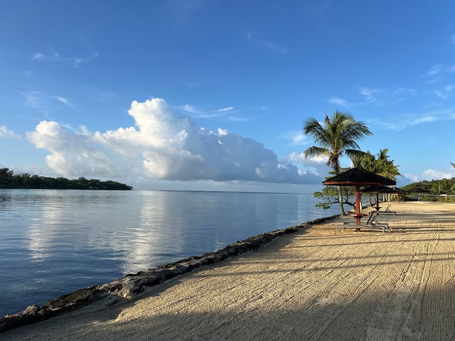 A serene beach view with palm trees and a hut at Warwick Le Lagon.