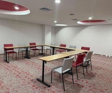 Mesas de reuniones en forma de U con sillas rojas y grises sobre alfombra estampada en Sala Fagua de Unika Hotels