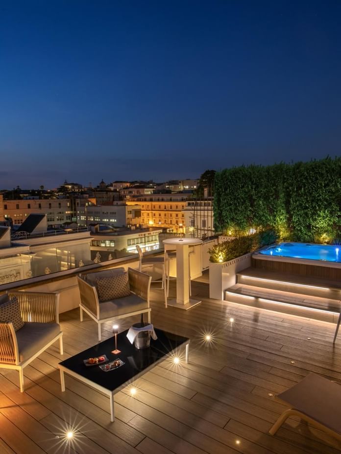 Rooftop terrace with a jacuzzi and cozy seating, surrounded by lush greenery and offering city views at The Glam Hotel