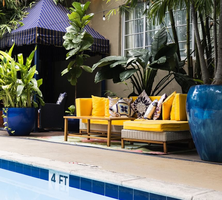 Vibrant poolside lounge at Riviera Hotel South Beach featuring yellow sofas, blue planters, and a striped cabana tent