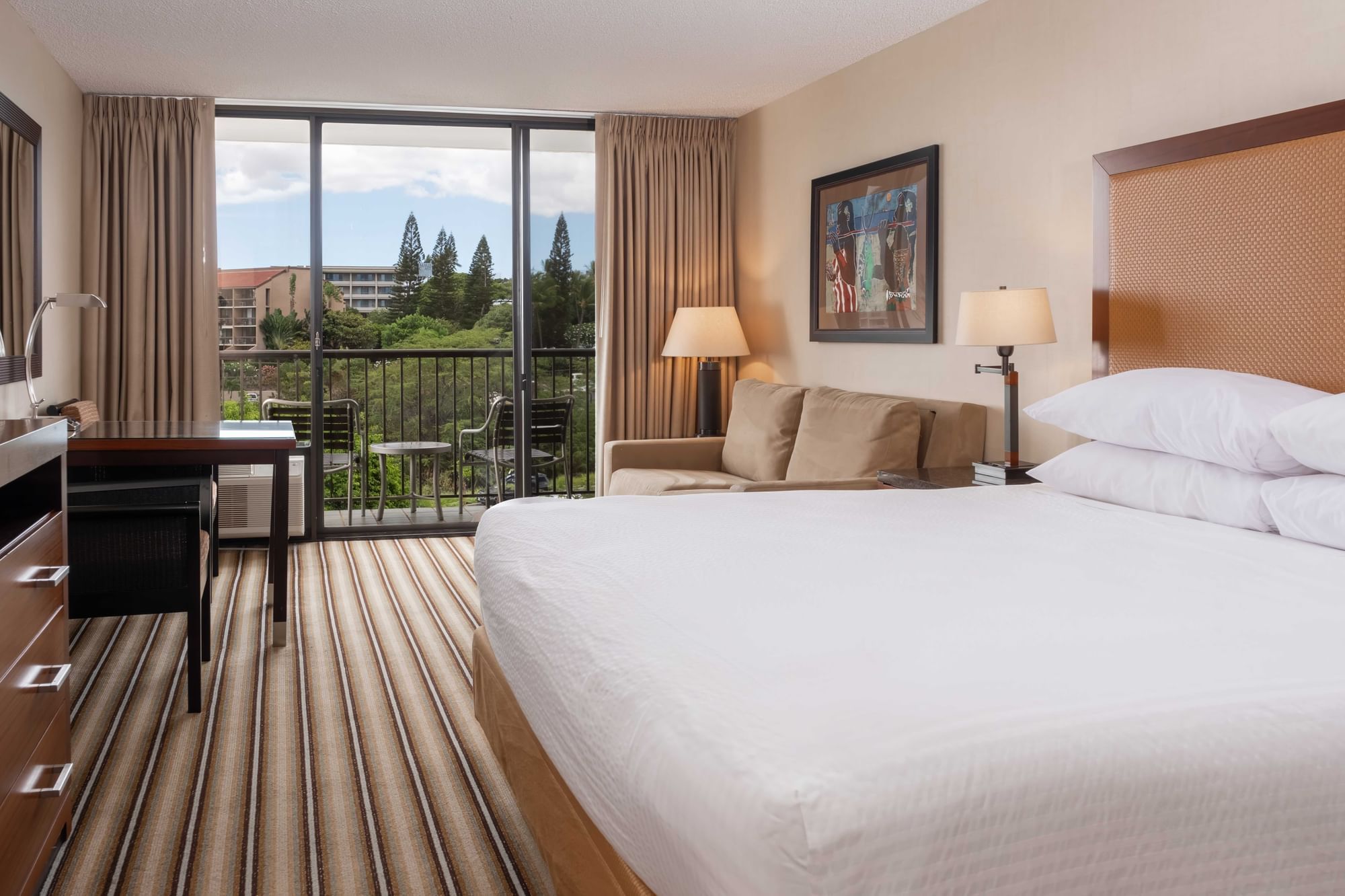 A hotel room with a large bed, sofa, desk, and balcony with a mountain view.