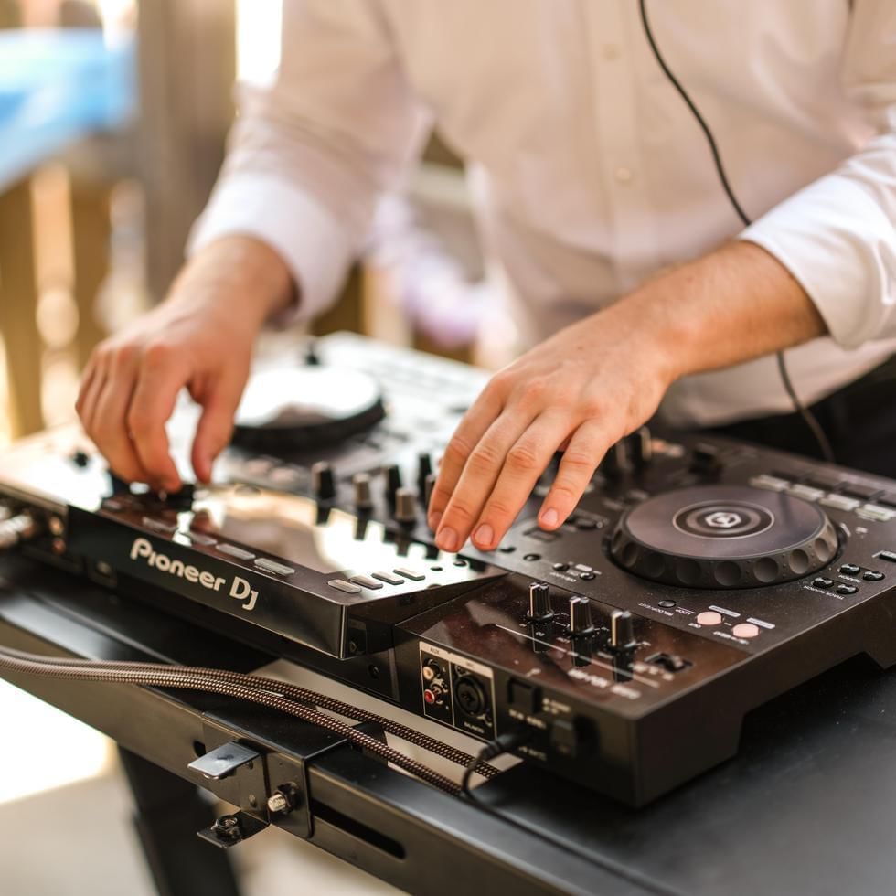 A person wearing a white shirt operates a Pioneer DJ mixer with headphones on.
