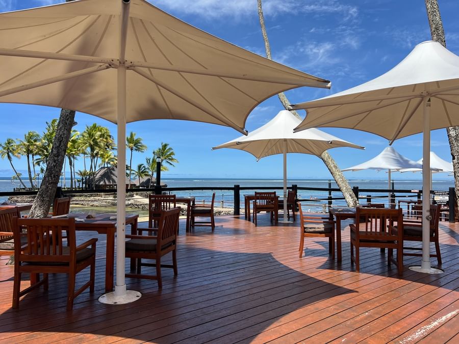 Wooden deck with tables and chairs under umbrellas at Warwick Fiji Resort and Spa.