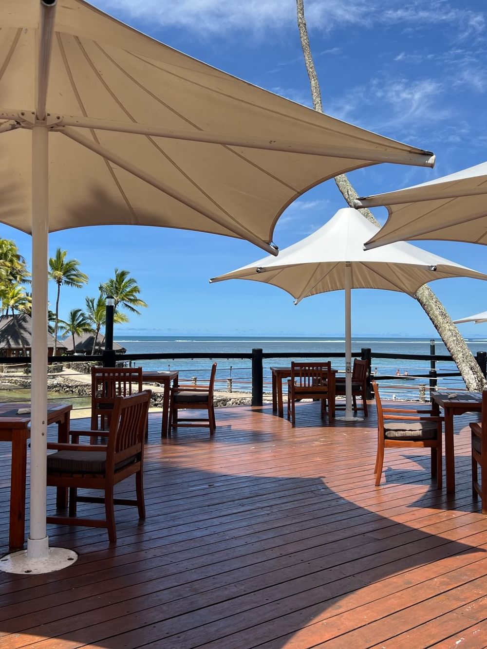 Outdoor tables and chairs under large umbrellas with ocean view at Warwick Fiji Resort and Spa in Korolevu.