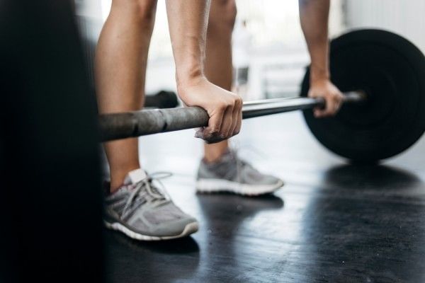 Close up of a barbell on the gym floor with someone reaching towards it.