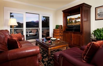 Living room with leather couches and a balcony with a mountain view in Presidential Cottage at The Stanley Hotel