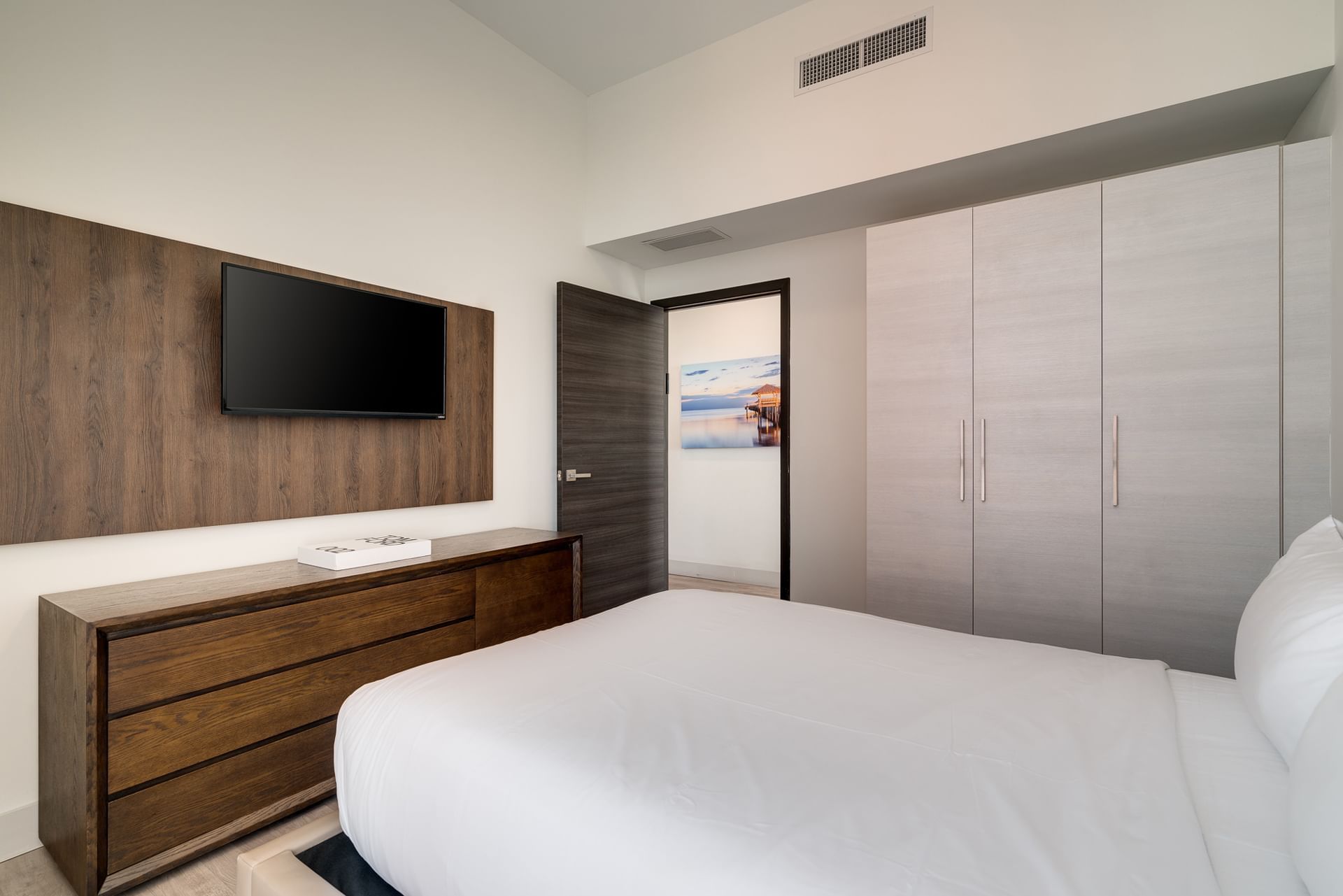 A modern hotel room with a bed, TV, closet, and dresser.