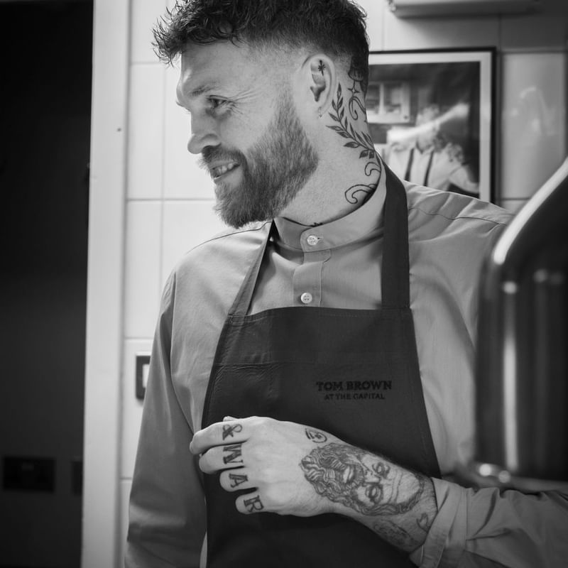 Chef in apron smiles while working in the kitchen, showcasing tattoos at Warwick Hotels and Resorts