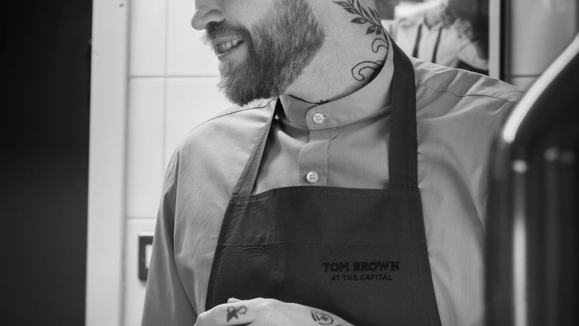 Chef in apron smiles while working in the kitchen, showcasing tattoos at Warwick Hotels and Resorts