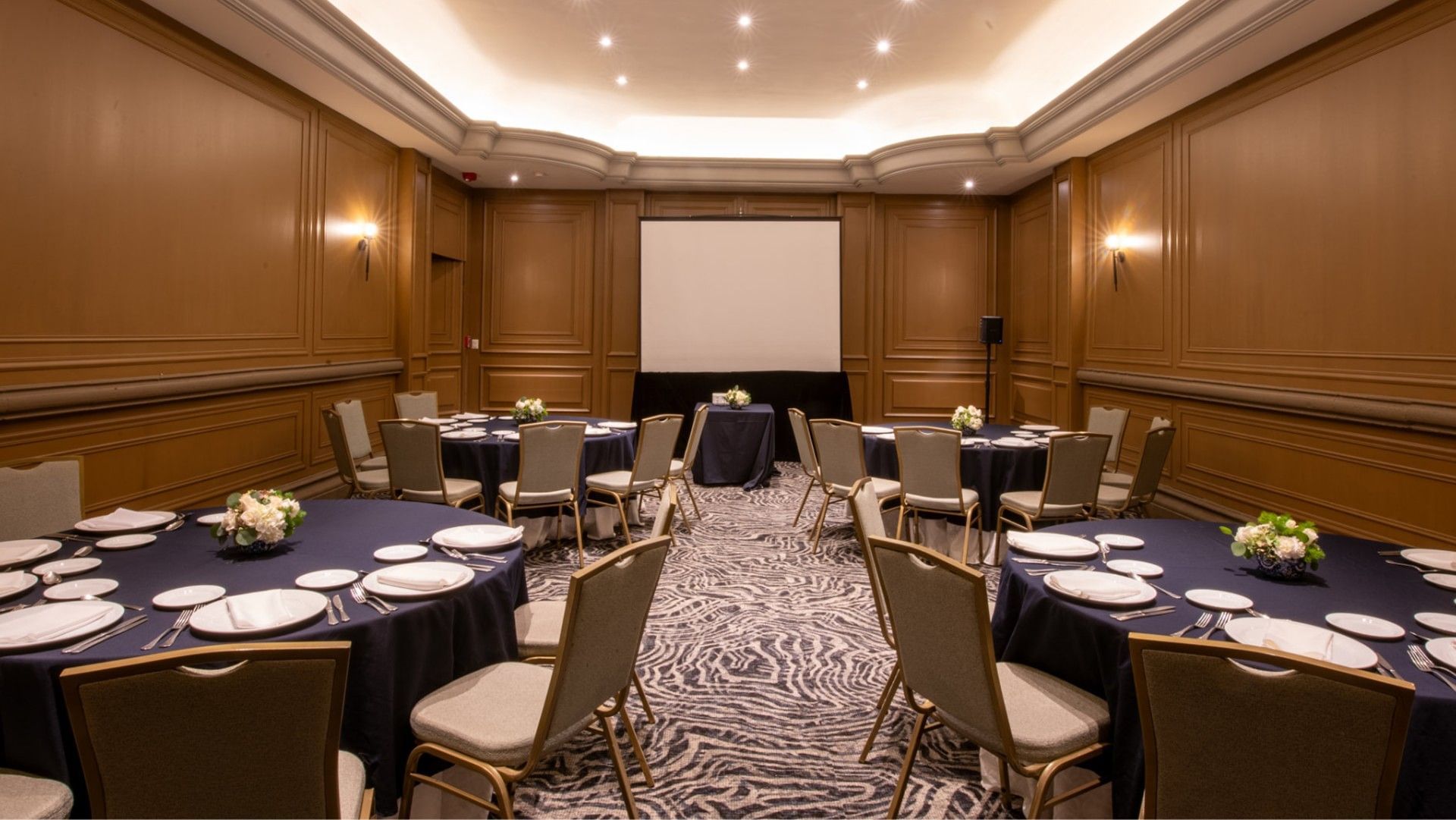Salon Virreinal with round tables, a projection screen, and patterned carpet at Quinta Real Monterrey