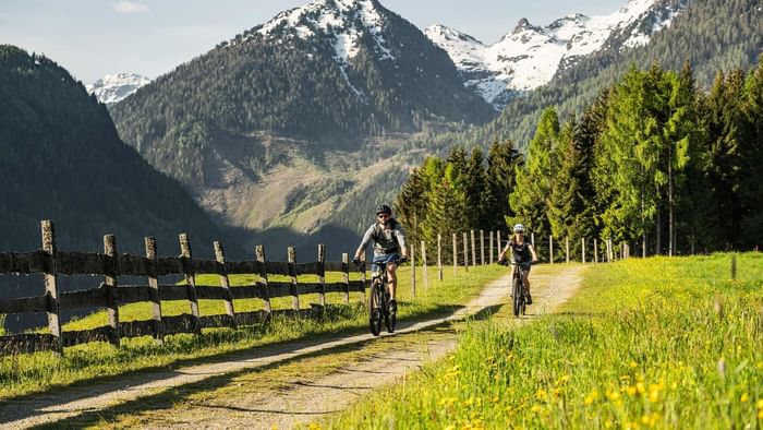 Couple riding on a mountain trail with snowy peaks in the background near Falkensteiner Hotel Schladming