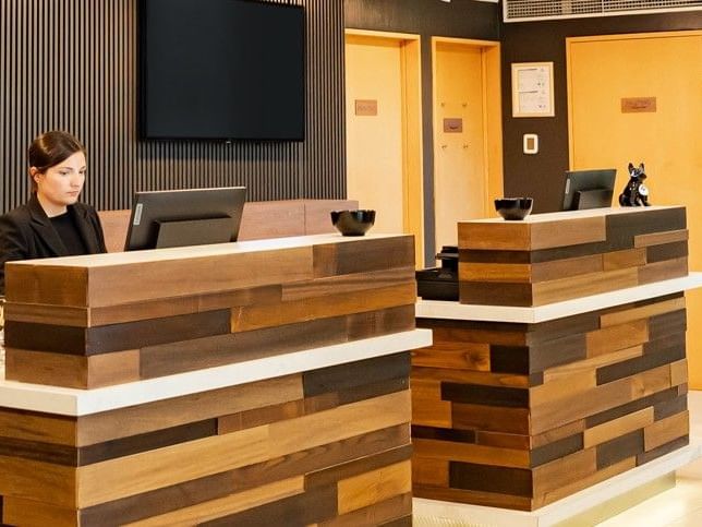 Mujer detrás del mostrador de recepción de madera del hotel HCC Costanera Concepción.