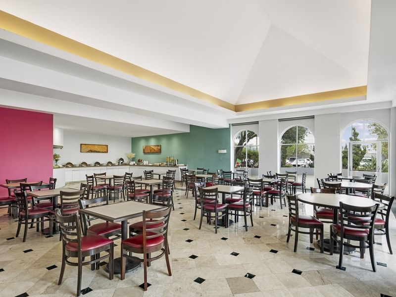 Luminoso comedor en Fiesta Inn Express Nuevo Laredo con varias mesas, sillas rojas y área de buffet