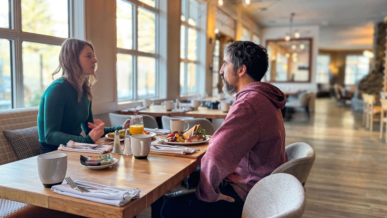 Two people are seated at a table in a restaurant, with food and drinks present.