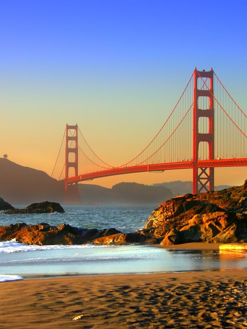 Golden Gate Bridge at sunset with rocky shoreline and ocean waves in San Francisco.