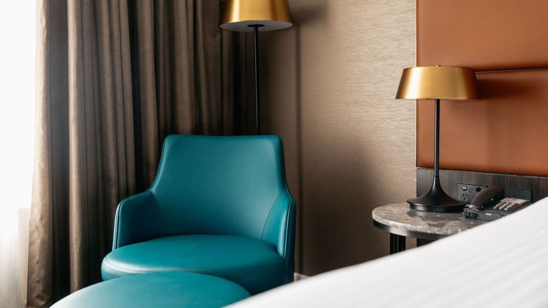 Hotel room with blue chair, gold lamps, white bed, and brown curtain.