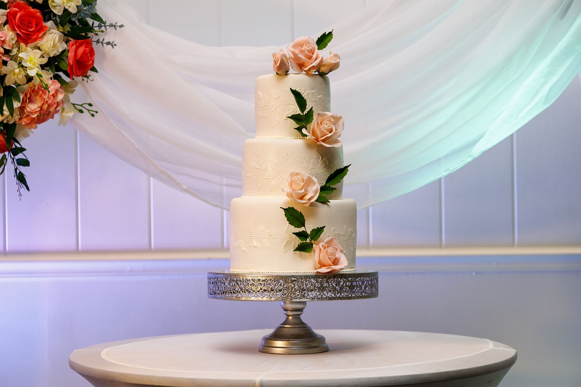 Four-tier wedding cake with peach roses on a silver stand at Warwick Hotels and Resorts