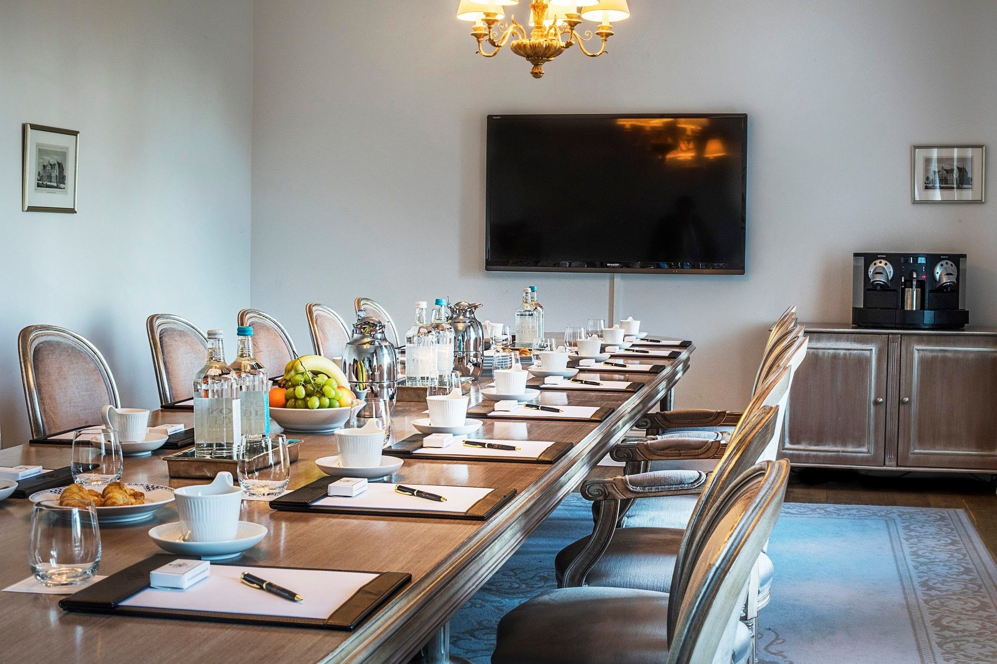 Close-up of a long conference table with water bottles & coffee cups and wall-mounted TV at Warwick Denmark