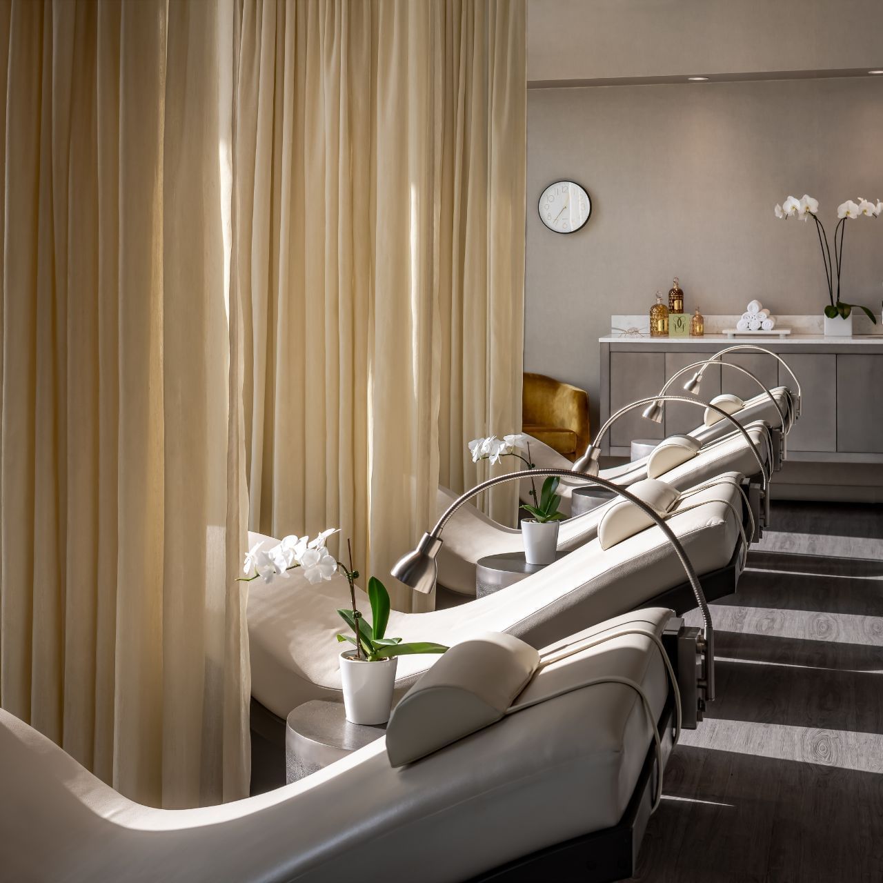 White spa loungers arranged by orchids and beige curtains under curved reading lamps in Guerlain Spa at Hotel X Toronto
