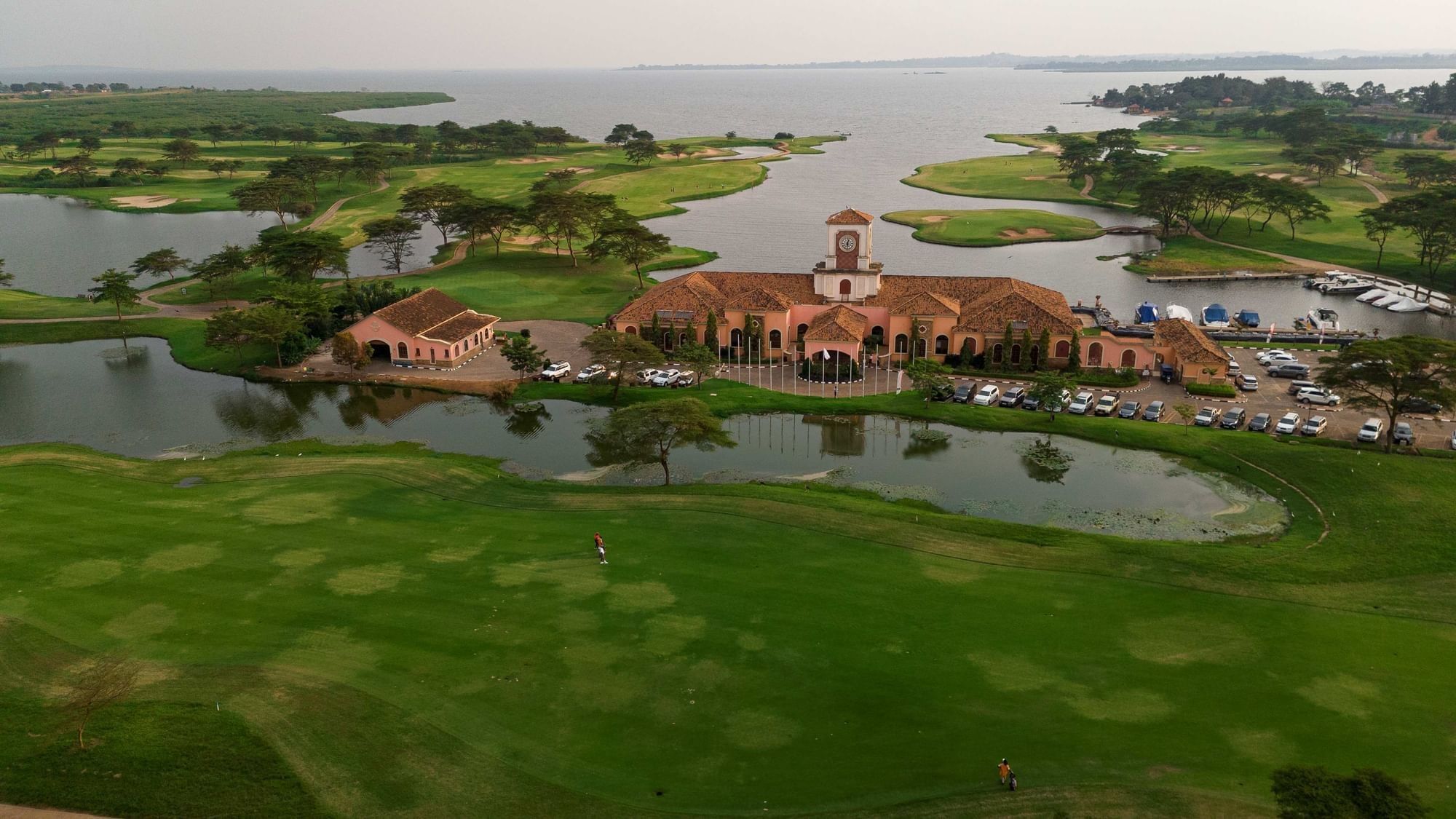 Aerial view of golf course surrounding terracotta-roofed clubhouse beside lake near Lake Victoria Serena Golf Resort & Spa