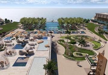 An aerial view of the resort with pools, palm trees, and ocean backdrop.
