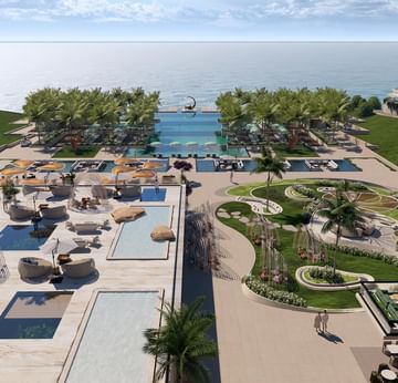 An aerial view of the resort with pools, palm trees, and ocean backdrop.