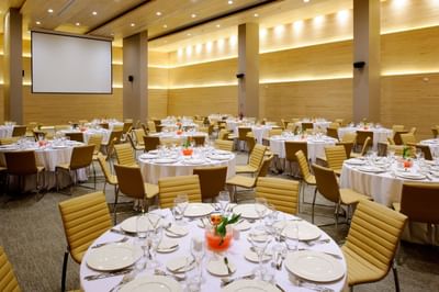 Mesas de banquete frente a gran pantalla de proyección en Salón Mayo en NOI Vitacura, Santiago, Chile