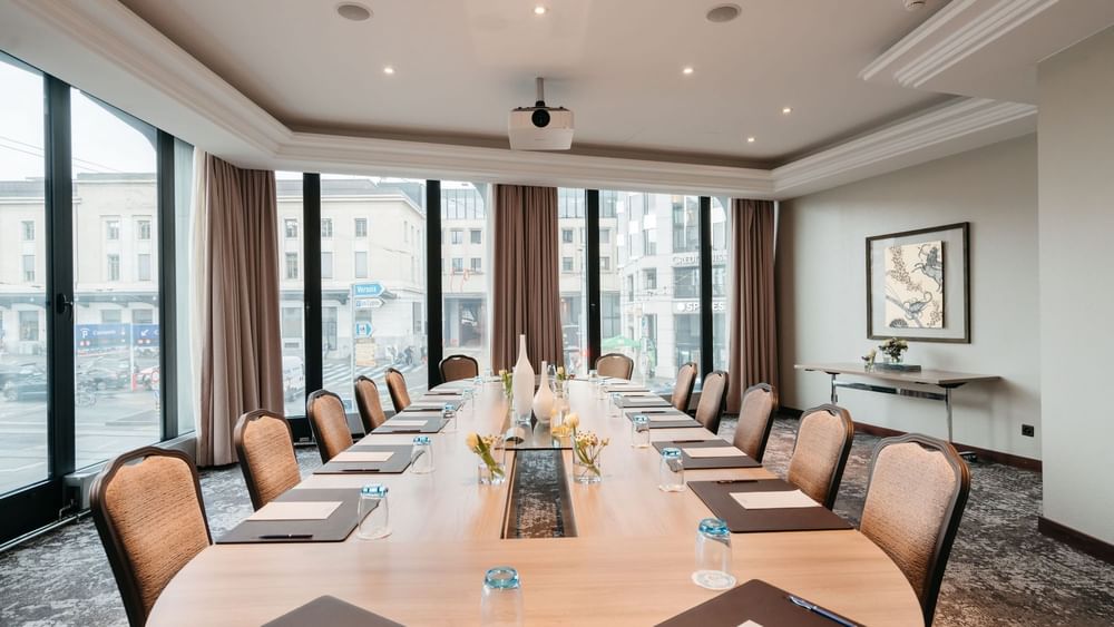 Long wooden table by tan chairs under a projector in Rigi at Warwick Geneva