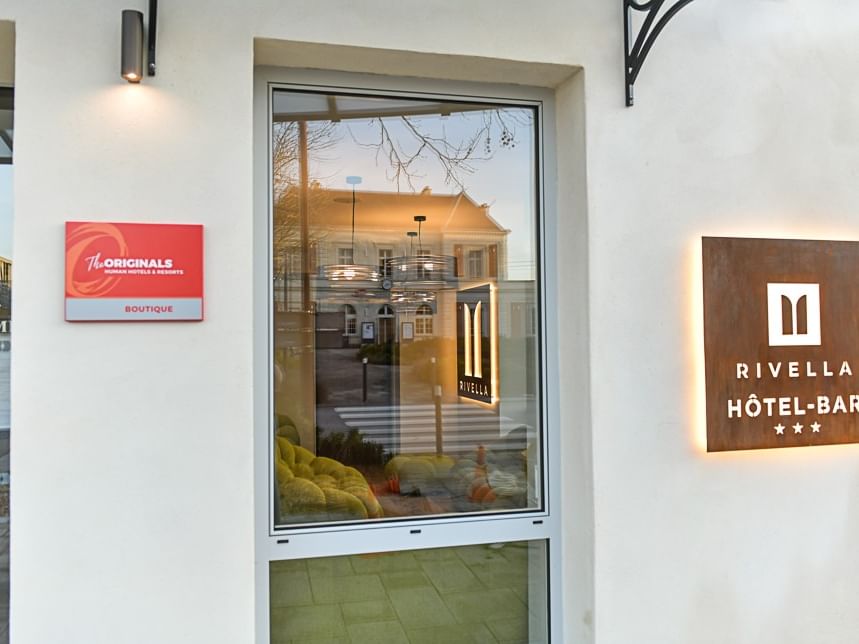 Entrée de l'Hôtel-Bar Hôtel Rivella avec panneaux lumineux et vitre réfléchissante.